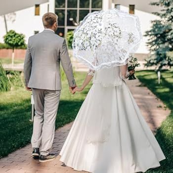 Brudpar går hand i hand, bruden håller ett vitt spetsigt paraply.